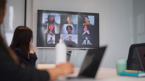 Image of hybrid training with employees in a classroom and participants on a screen in a Zoom meeting. 